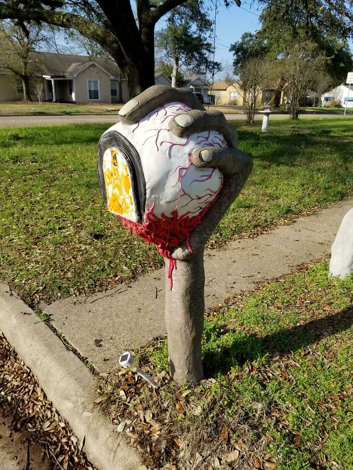 Creative and cool mailbox shaped like a bloody eyeball held by a hand in a suburban neighborhood setting.