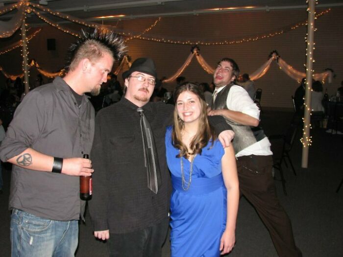 Group of friends posing for a photo with a man photobombing and making a funny face at a decorated event.