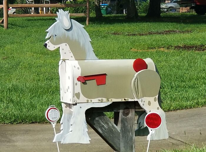 Mailbox designed as a white horse with red flag and reflectors, a creative and cool mailbox spotted outdoors on a green lawn.