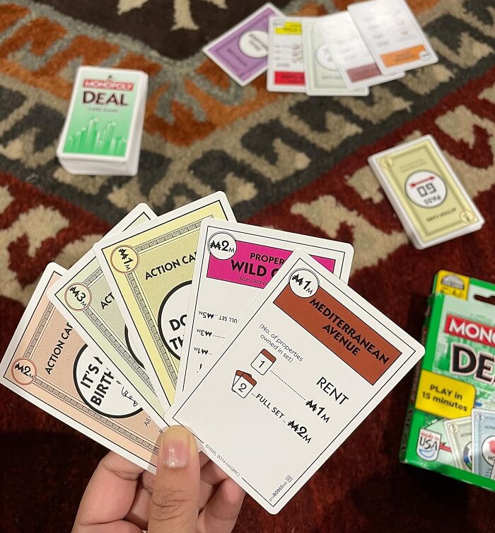 Hand holding Monopoly Deal cards on a patterned rug, a fun game idea for stocking stuffers gift giving.