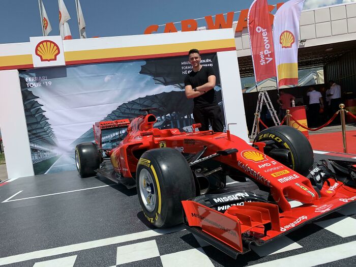 Man standing next to a red Formula 1 car, showcasing a big dream turned into reality and inspiring the internet.