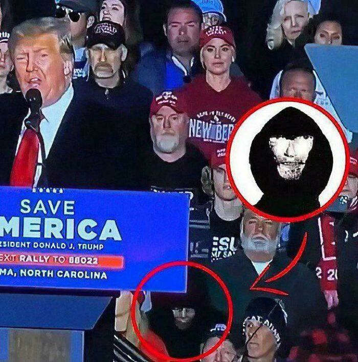 Crowd at a rally with a mysterious figure in a black hoodie resembling a skull face, highlighting things that look like others.