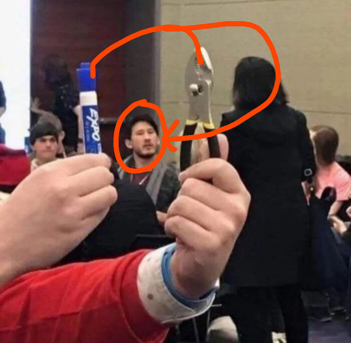 Person holding marker and pliers in front of a man whose face and wrench together look like a humorous visual illusion.