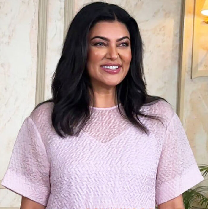 Sushmita Sen smiling indoors, wearing a light pink textured top, reflecting her bio and career highlights.