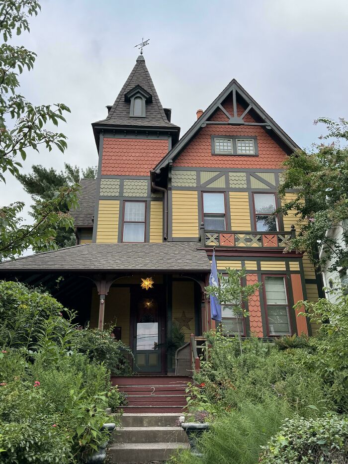 Victorian-style beautiful old house with intricate craftsmanship, vibrant colors, and lush greenery surrounding the entrance steps.