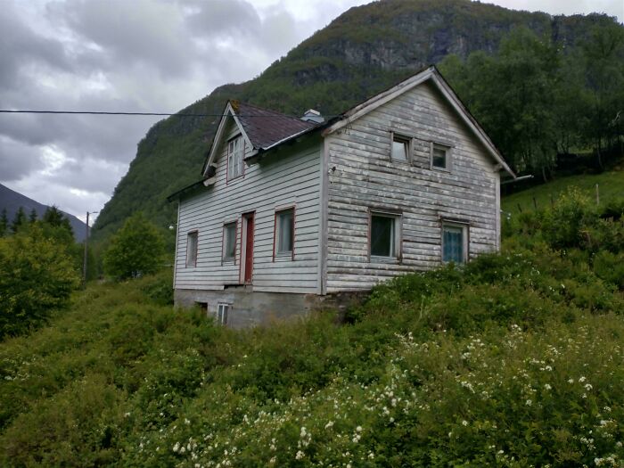 Weathered old house surrounded by greenery, showcasing craftsmanship and timeless architecture in a natural mountain setting.