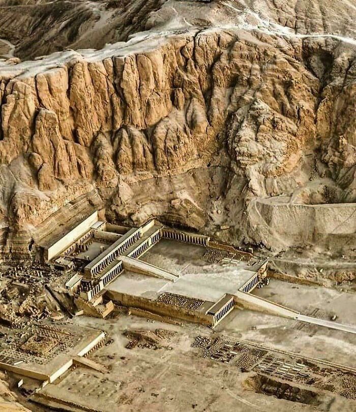 Aerial view of archeological site with ancient ruins and structures carved into rocky desert landscape.