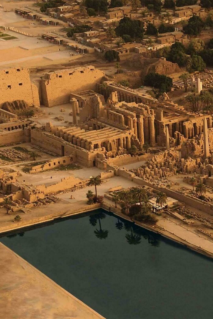 Aerial view of ancient archeology site with ruins and columns beside a reflective water pool in desert area.