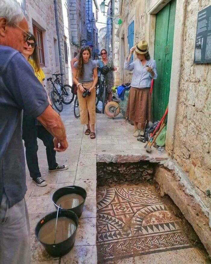 Archeology enthusiasts examining an ancient mosaic floor uncovered during an archeological dig in a narrow stone street.