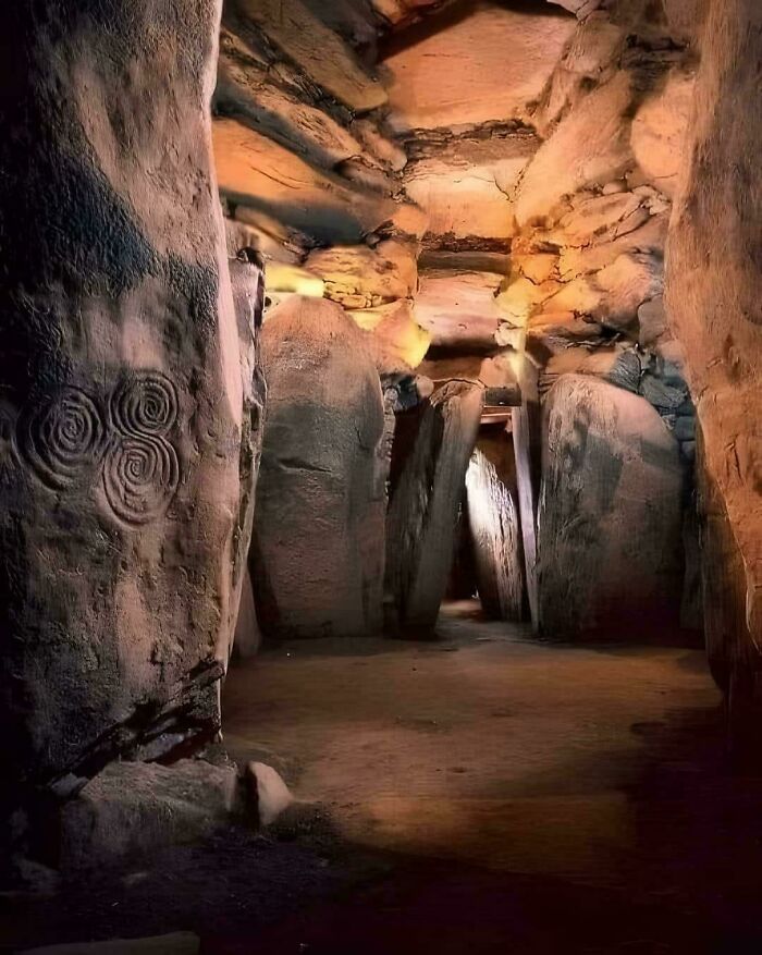 Ancient archeology site with stone pillars and carvings inside a dimly lit, narrow archaeological chamber.