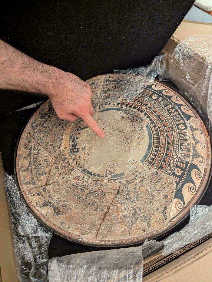 Hand pointing at a c*****d ancient ceramic artifact with detailed patterns, showcasing fascinating archeology finds worldwide.