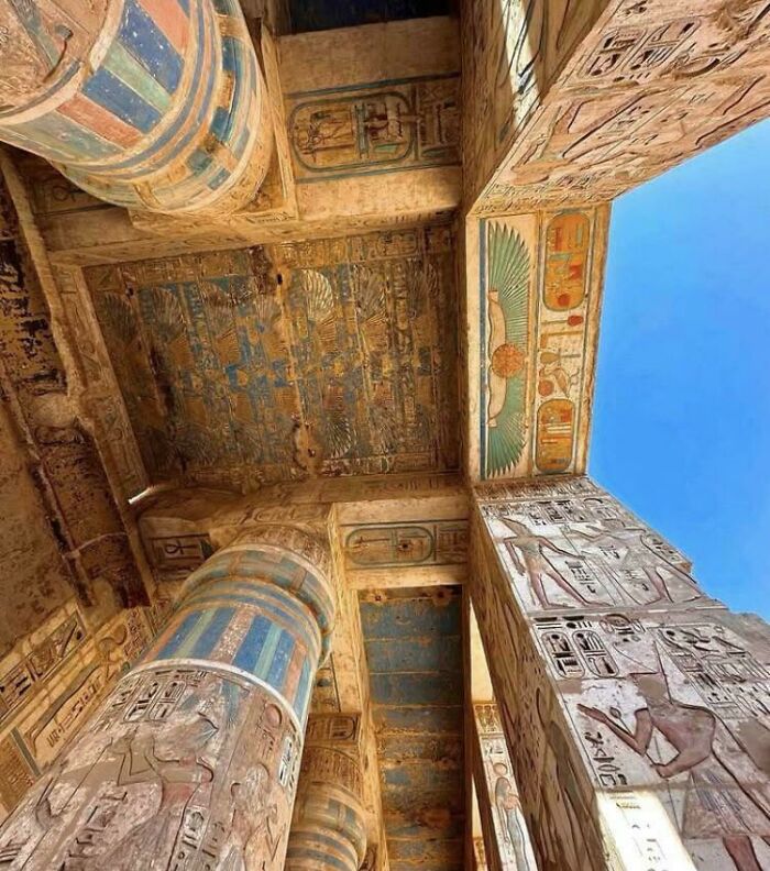 Ancient Egyptian temple columns and ceiling decorated with detailed hieroglyphs and colorful artwork from archeology finds.