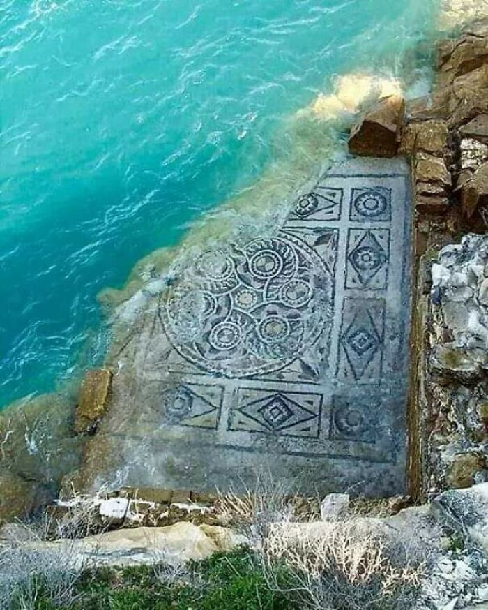 Ancient mosaic partially submerged in water showcasing intricate archeology patterns on a rocky coastal site.