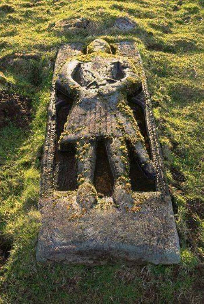Ancient stone effigy of a knight discovered during archeology excavations covered in moss on grassy ground.