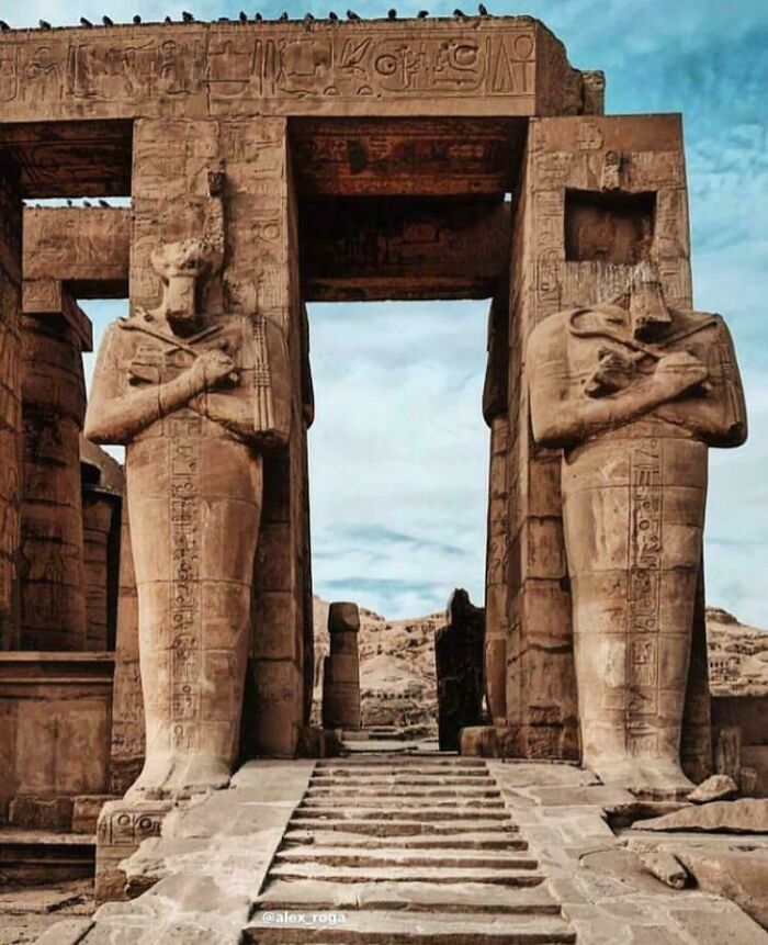 Ancient archeology site with large stone statues and hieroglyphs at an Egyptian temple entrance under blue sky.
