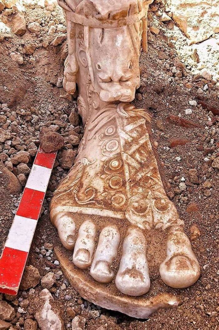 Intricately carved ancient stone foot sculpture partially unearthed during archeology excavation site.
