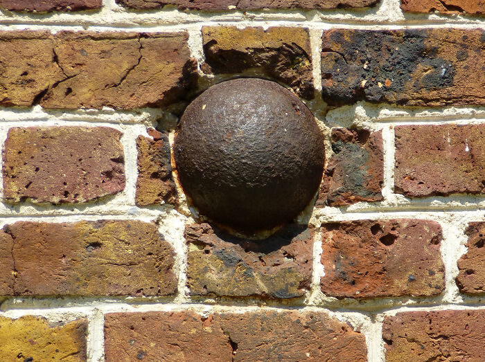 Old iron cannonball embedded in a weathered brick wall, an intriguing archaeology find from around the world.