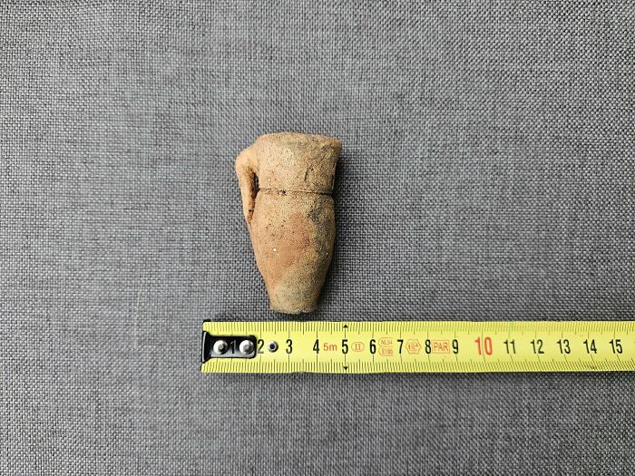 Small ancient pottery artifact placed next to a measuring tape, showcasing an archeology find from around the world.