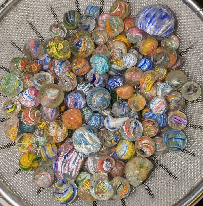 Colorful ancient glass marbles discovered in archeology, showcasing fascinating finds from around the world in a metal sieve.