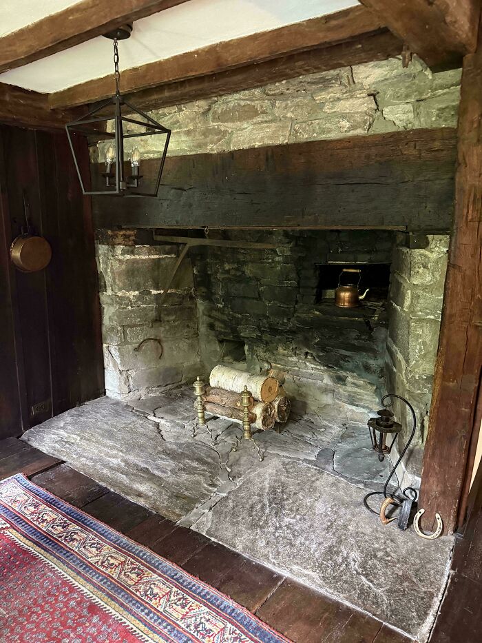 Rustic stone fireplace with wooden beams and vintage tools in a beautiful old house showcasing timeless craftsmanship.
