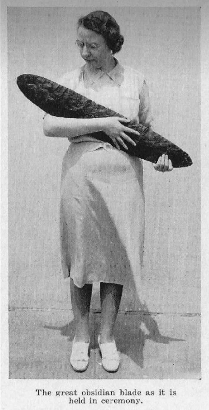 Woman wearing a dress holding a large obsidian blade in an archeology find from around the world ceremony.