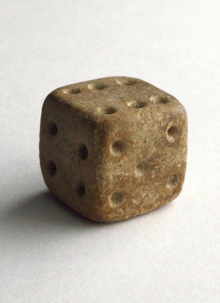 Ancient carved stone die with worn pips, a fascinating archeology find from around the world displayed on a white surface.