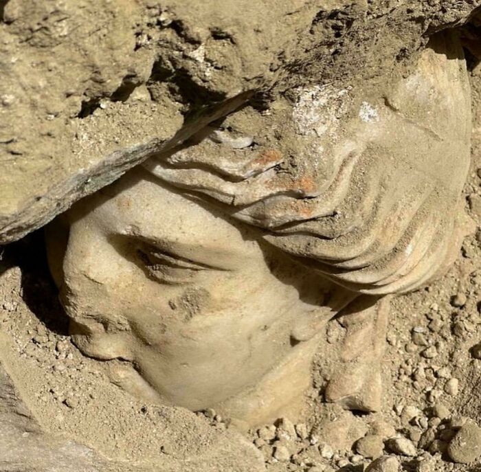 Ancient sculpture partially unearthed in dirt showing detailed human face, a fascinating archaeological find from around the world.