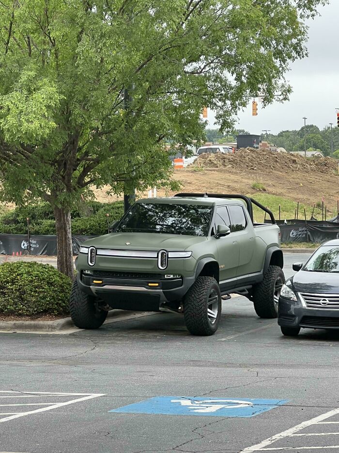 Matte green truck with oversized tires trying to look cooler but giving an impression of stupidity on wheels in parking lot.