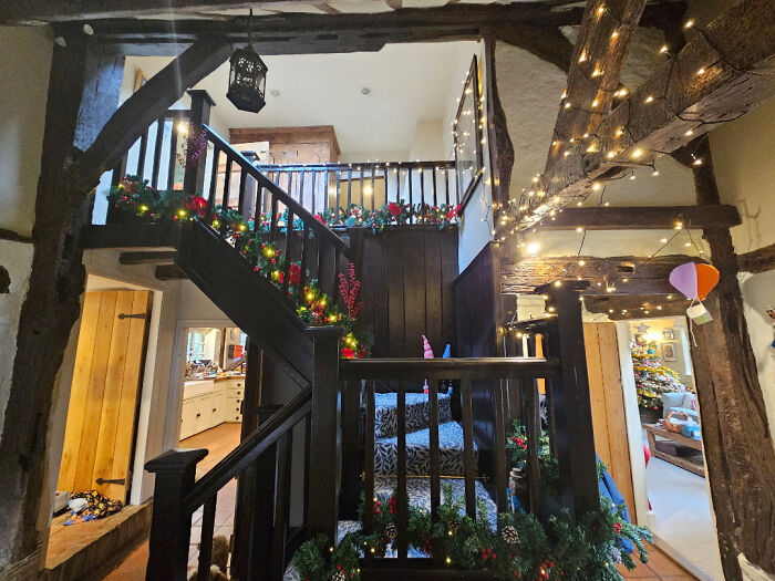 Cozy old house interior with wooden beams and staircase decorated with festive lights and greenery showing craftsmanship.