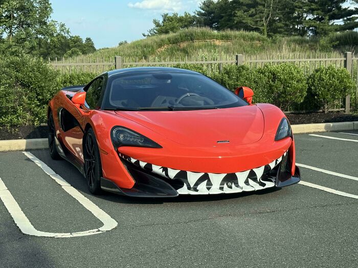 Red sports car with a large shark mouth decal on the front bumper, an example of stupidity on wheels customization.