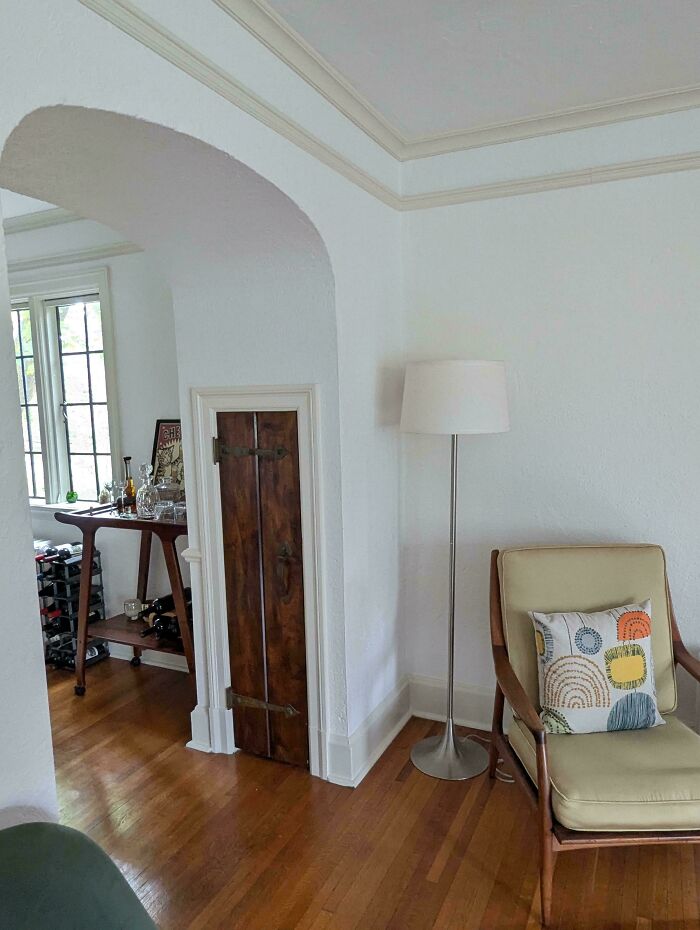 Cozy corner in a beautiful old house featuring vintage wooden door, modern floor lamp, and mid-century chair with decorative pillow.