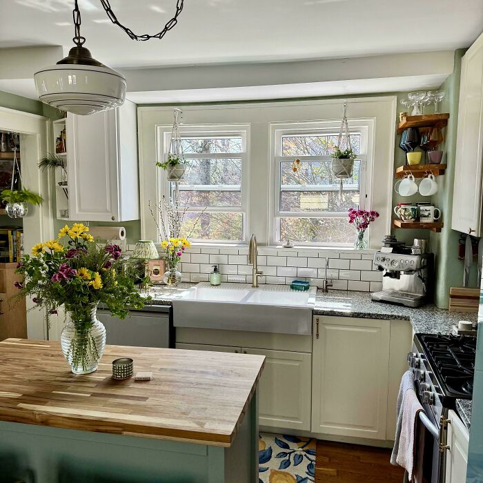 Cozy kitchen in a beautiful old house with farmhouse sink, wooden island, hanging plants, and vintage craftsmanship details.