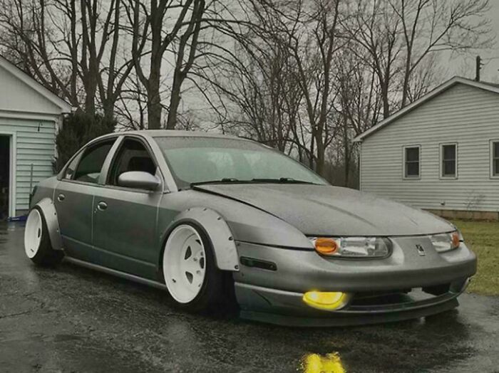 A customized car with oversized white rims and extended fenders, an example of stupidity on wheels modifications.