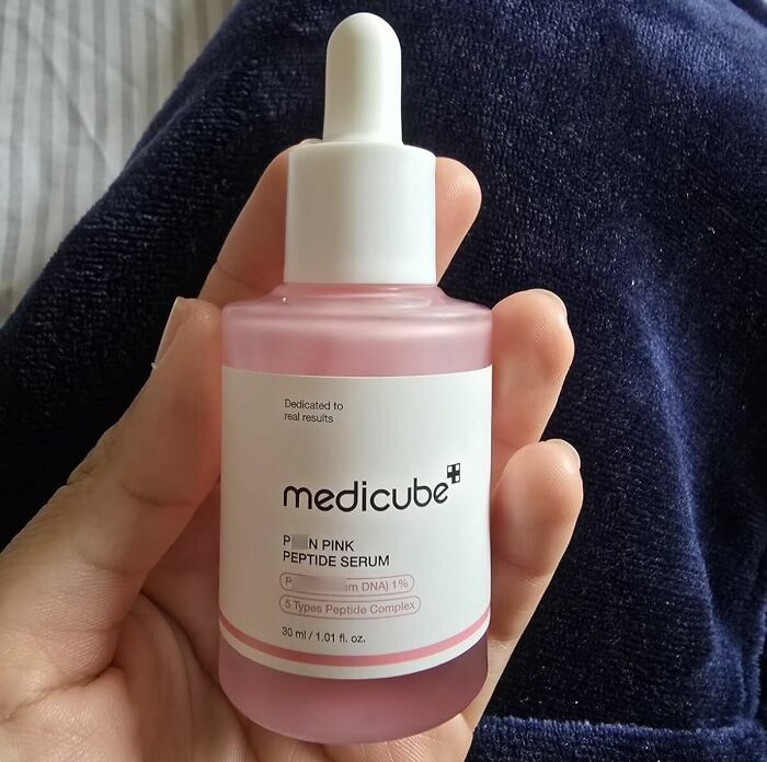 Hand holding a pink Medicube peptide serum bottle, one of the holy grail beauty deals for Black Friday restocking.
