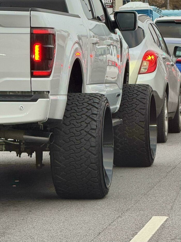 Pickup truck with excessively wide tires parked behind small cars, showcasing a failed attempt at making the car cooler.