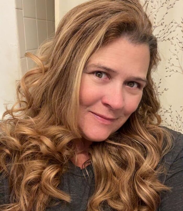 Woman with long curly hair taking a selfie showcasing beauty and skincare for Black Friday restocking and holy grail deals.