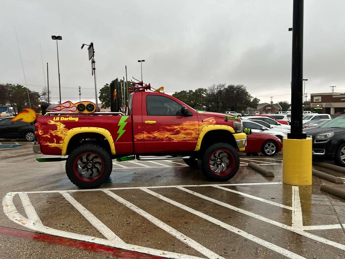 Red pickup truck with flame and lightning bolt decals and oversized speakers, an example of stupidity on wheels car modifications.