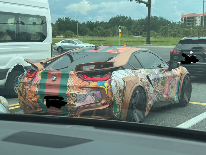 BMW with unusual floral and stripe design and custom body modifications showing car stupidity on wheels on the road.