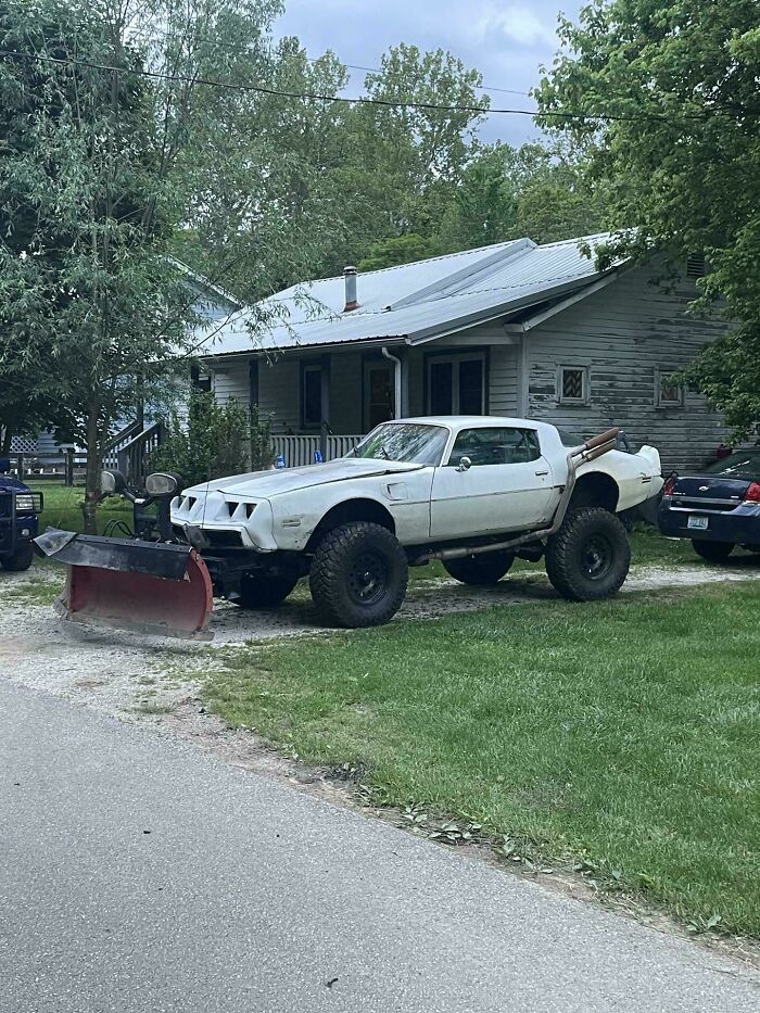 Modified car with off-road tires and a snowplow attachment, an example of stupidity on wheels and failed car coolness.