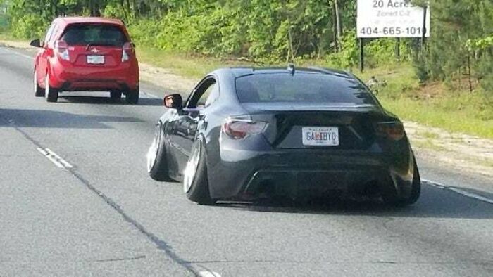 Black car with extremely wide tires and negative camber driving on a road, showing a failed attempt to make the car cooler.