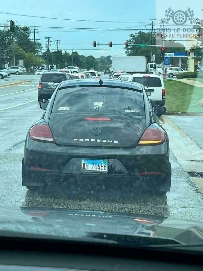 Car with altered badge spelling "Pooorsche" instead of Porsche, showcasing stupidity on wheels in a traffic jam.