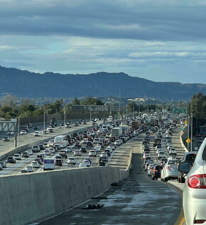Heavy Miami highway traffic during a cloudy day with mountains in the background and many cars on the road.