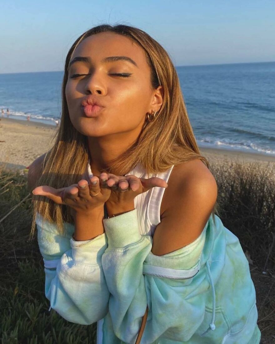Young woman blowing a kiss at the beach, illustrating different types of kisses in history and culture.