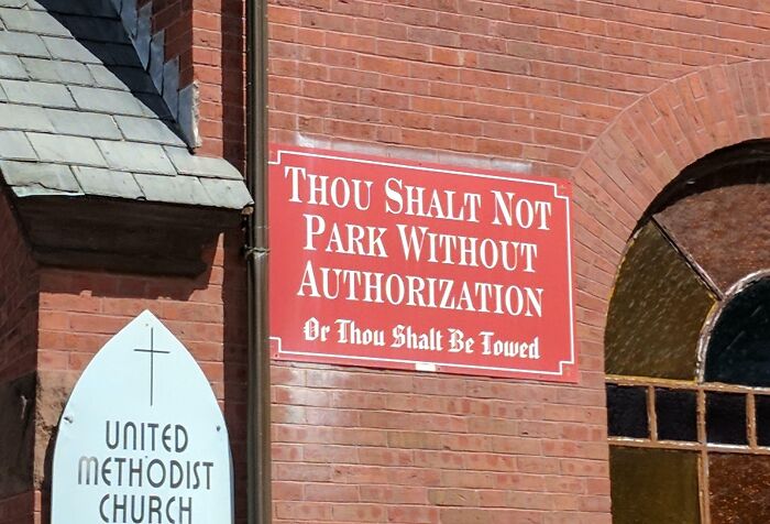 Red church sign with a humorous message about parking outside a United Methodist Church building.