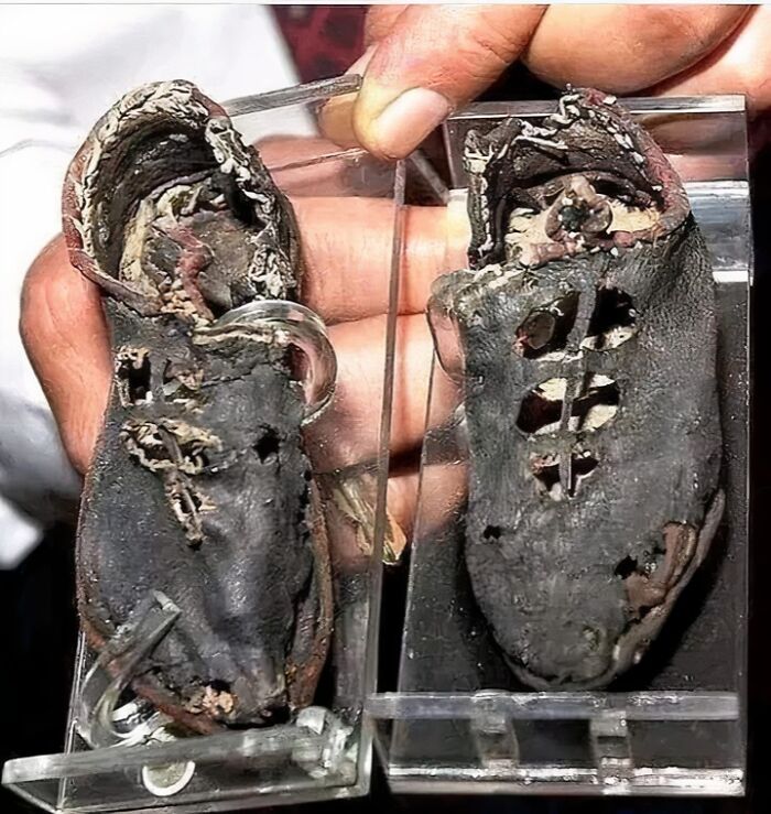Worn ancient leather shoes discovered in archeology find displayed on clear holders, showing detailed craftsmanship.