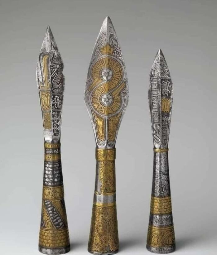 Three ornate ancient metal spearheads with intricate gold and silver archeology designs displayed on a neutral background.