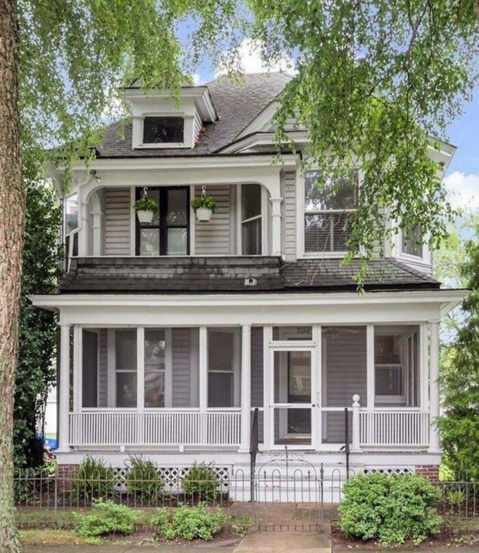 Beautiful old house with classic craftsmanship, featuring a spacious porch and detailed woodwork surrounded by greenery.