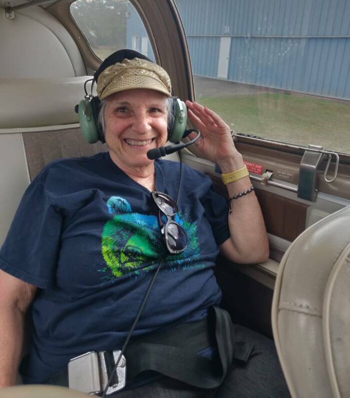 Elderly woman wearing headset and cap smiling inside a small aircraft, showing big and small dreams turned into reality.