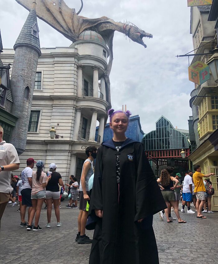 Young woman with purple hair in wizard costume beside dragon statue, showcasing dream-inspired creativity and imagination.