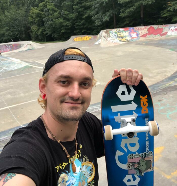 Young man smiling with a skateboard at a skate park, showcasing big and small dreams turned into reality.